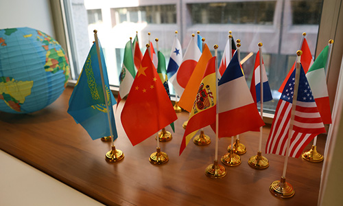 Mini flags from countries around the world stand displayed on a city windowsill with an inflatable globe next to them.