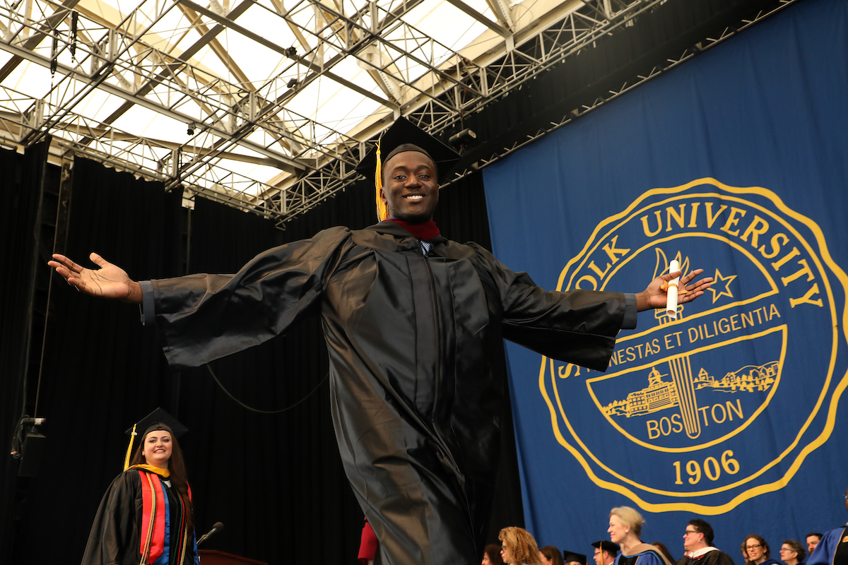Clevis Murray crosses the stage at the Commencement ceremony with his arm spread wide.