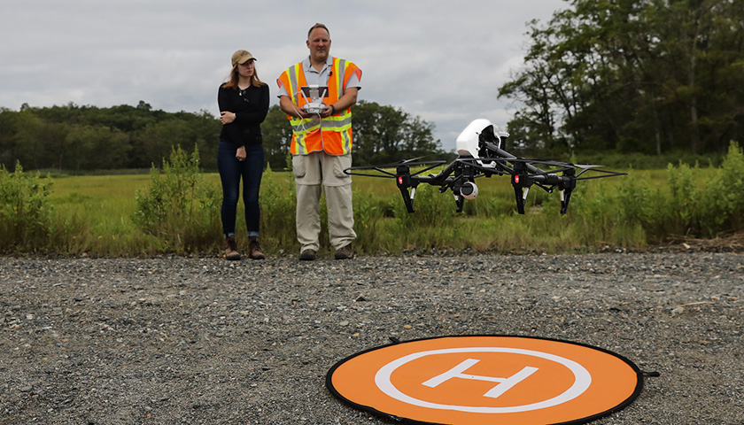 Instructor and student watch as drone takes off from orange launch pad