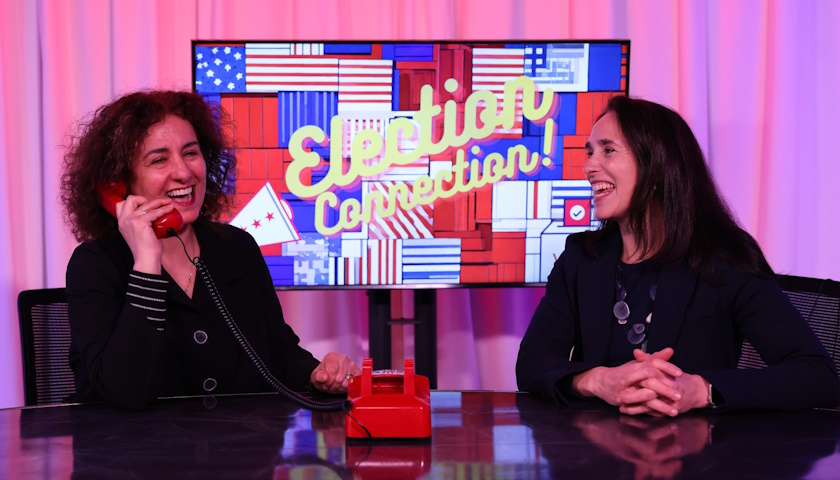 Shoshana Madmoni-Gerber (left) holds a red telephone as she and Rachael Cobb (right) laugh while sitting at a table in Suffolk's Studio 73 in front of a monitor that reads 'Election Connection'