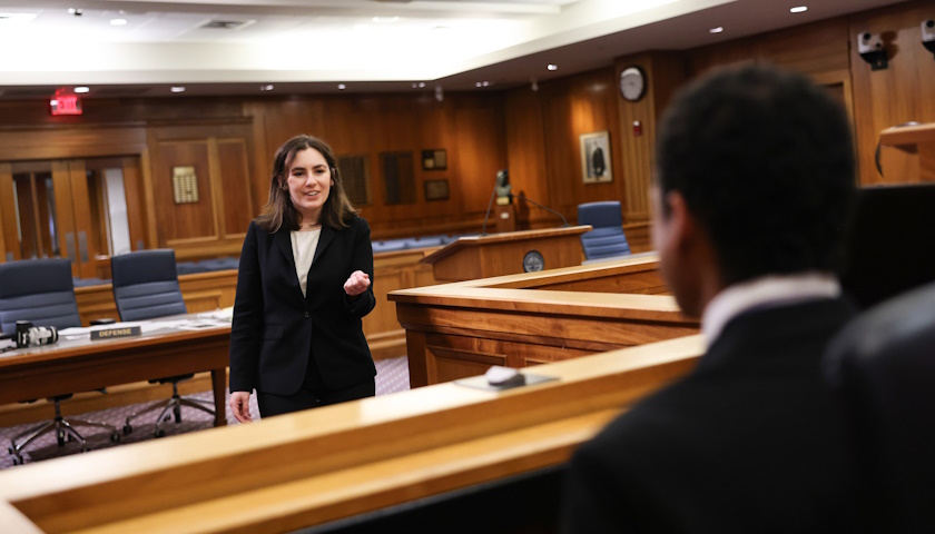 Brenna Koppel stands in one of Suffolk's mock courtrooms and points to her teammate, Stephen JIminez, on the witness stand