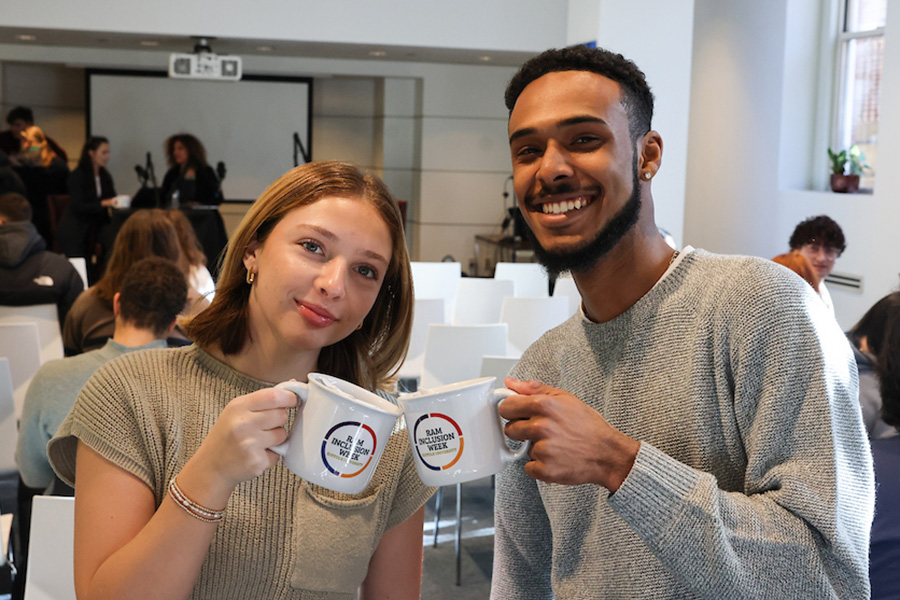 Two Suffolk students doing a "Cheers!" motion with two branded coffee mugs.