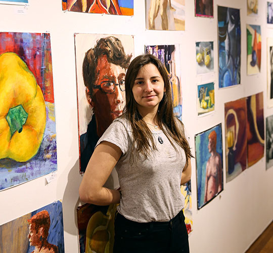 Student standing in front of a wall of hanging art