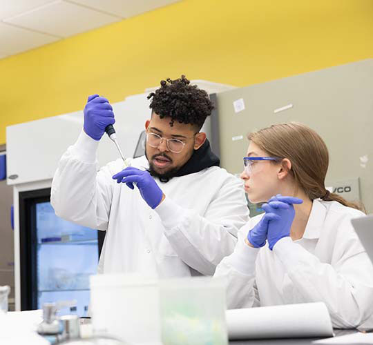 Two students performing experiment with a test tub whil wearing lab gear