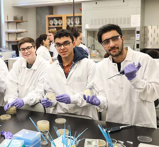 Three students in lab gear performing an experiment