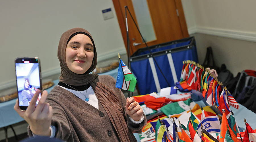 A Suffolk student at an international student event takes a selfie holding a small Uzbekistan flag