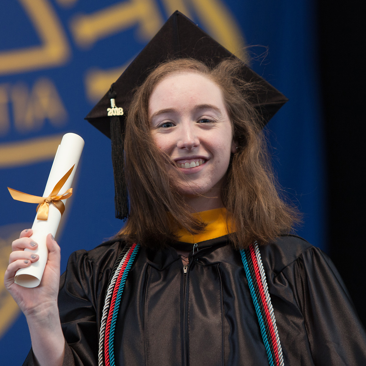 Ashley holding up her scroll while walking across the stage during Commencement.