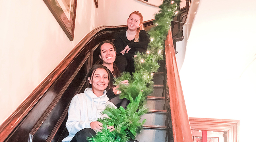 Three women sitting on stairs entwined with a green garland