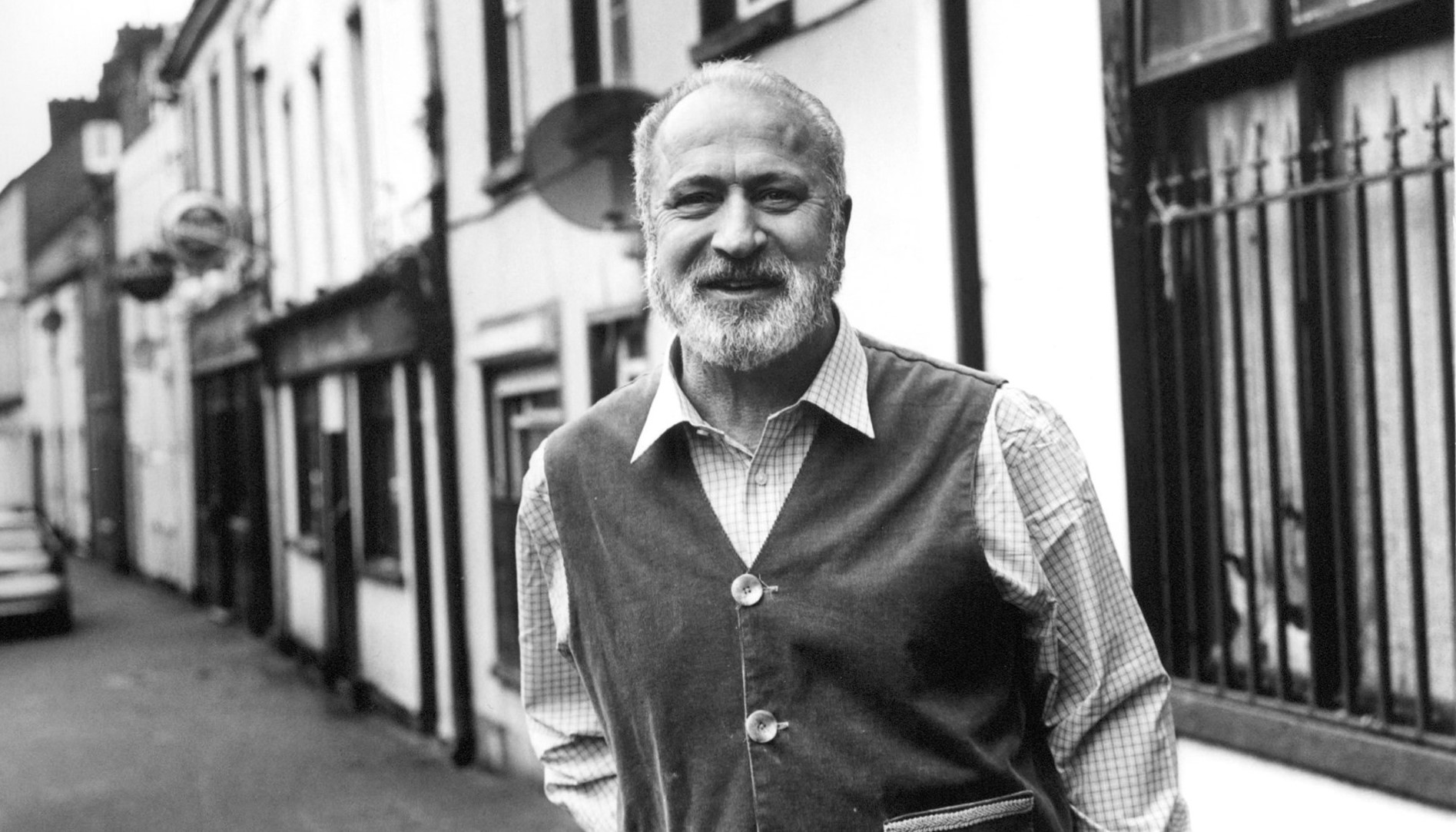 Black and white image of poet Greg Delanty on the street smiling