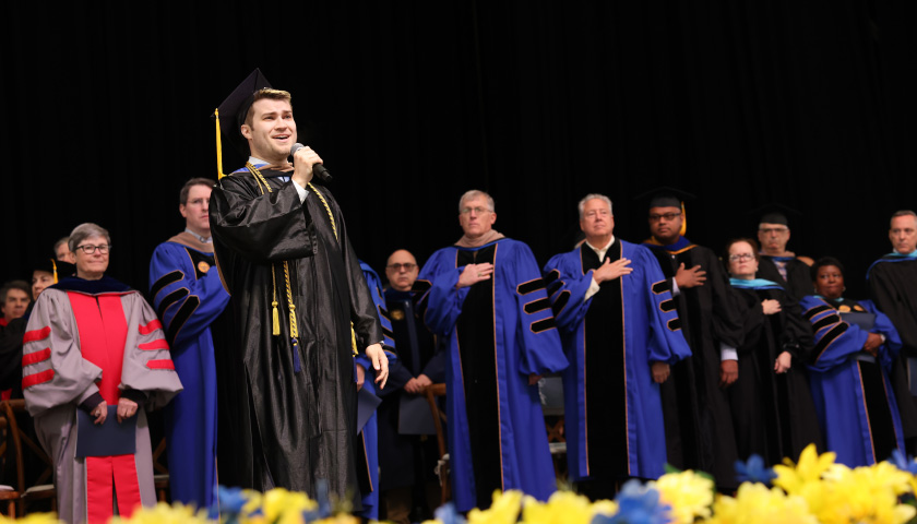 SBS graduate Connor Mudge sings the national anthem on stage during Commencement