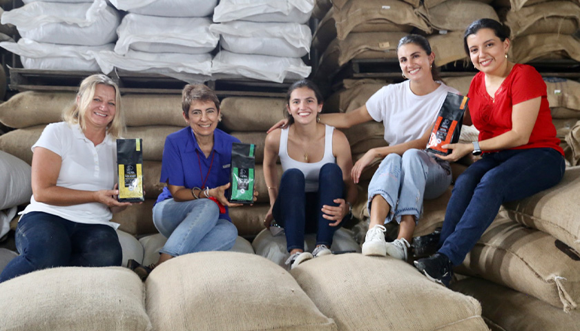 Annette Sachs and her sister, Claudia, sit on large bags filled with coffee beans, next to three of their suppliers: Carol Zbinden, Cecilia Genis, and Kathia Zamora.