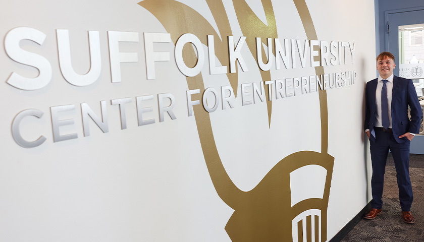 Noah Jones standing next to a wall-size sign for the Suffolk University Center for Entrepreneurship