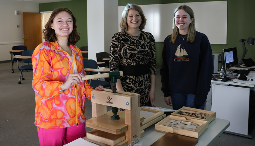 Maddie Stanley, Professor Hannah Hudson, and Matilyn Paul stand with the portable printing press