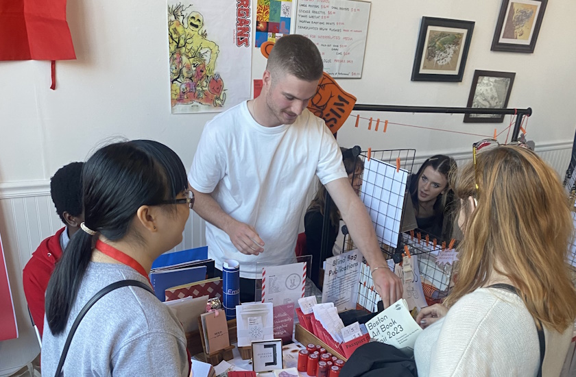 Student helps customers see work at the Suffolk table at the Boston Art Book Fair