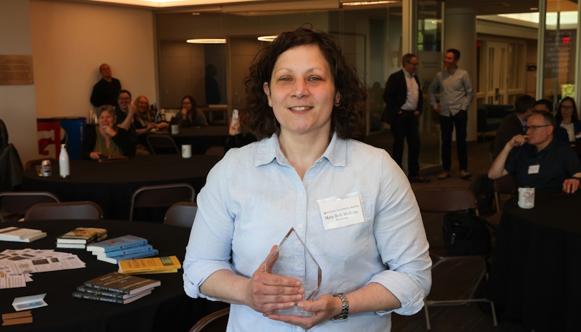 Mary Beth Medvide holds a glass award while standing in front of tables and books