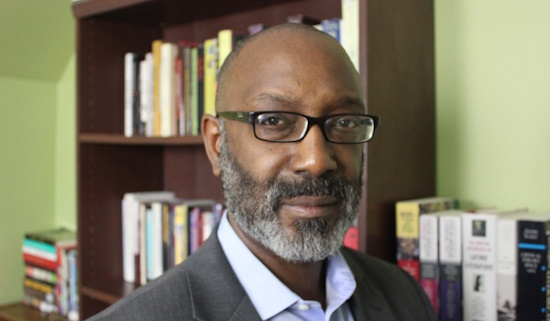 A portrait of Trent Masiki in front of a bookshelf