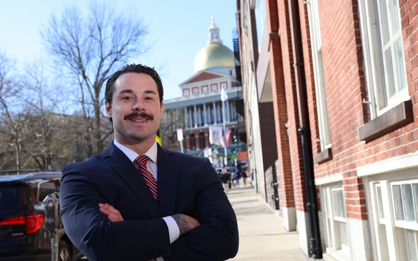 Cody Black stands outside in professional attire, arms crossed, with the Massachusetts State House in the background