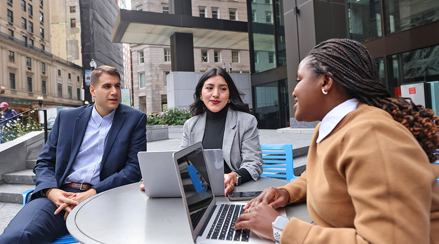 Three Graduate students meeting together at an outdoor table with a laptop.