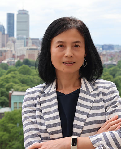 Dean Amy Zeng, smiling, indoors in peach colored jacket